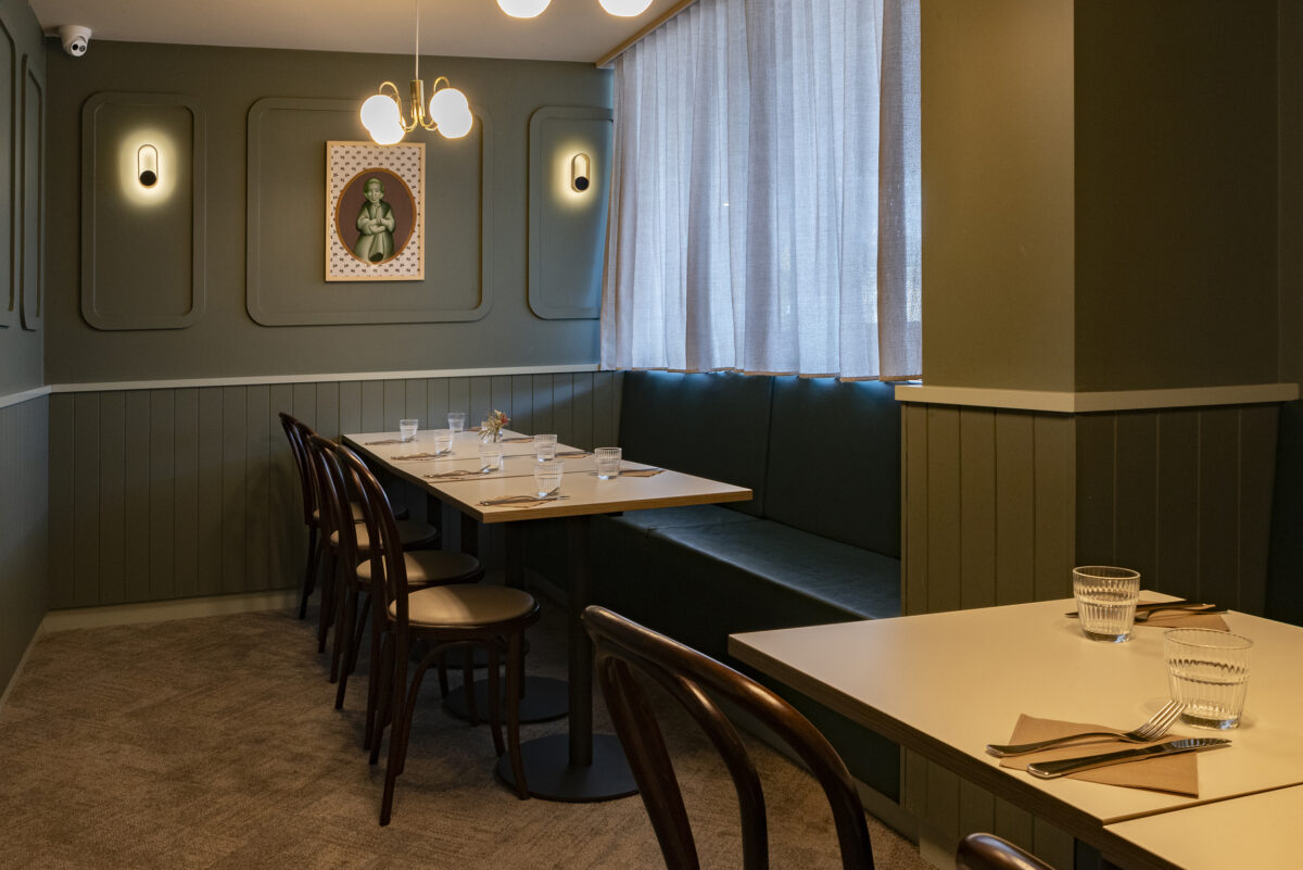 A soft, moody dining corner layered with panelling, muted greens and tailored banquette seating.