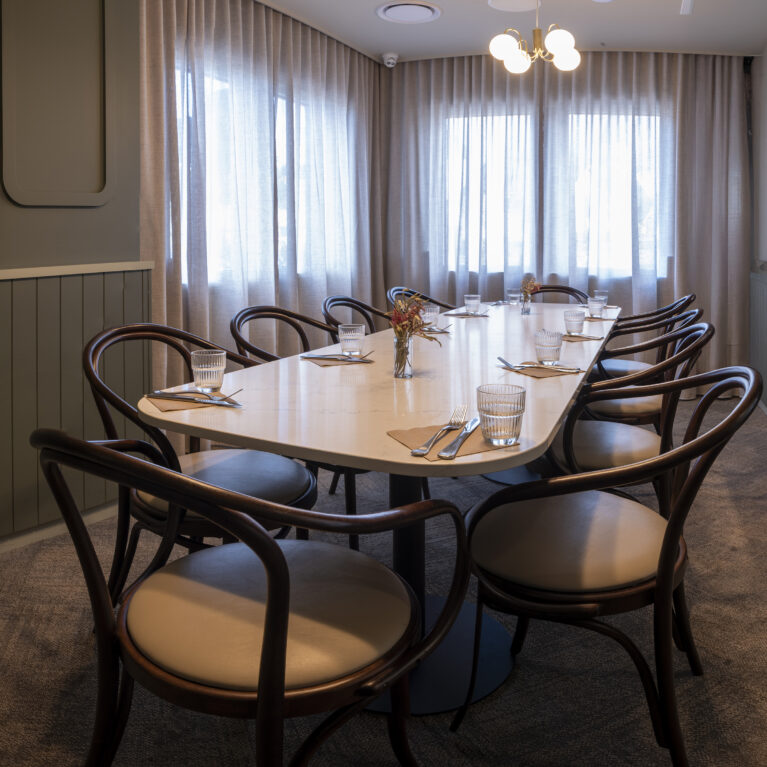 A refined private dining space centred around a sculpted stone-look table and enveloped in soft drapery.