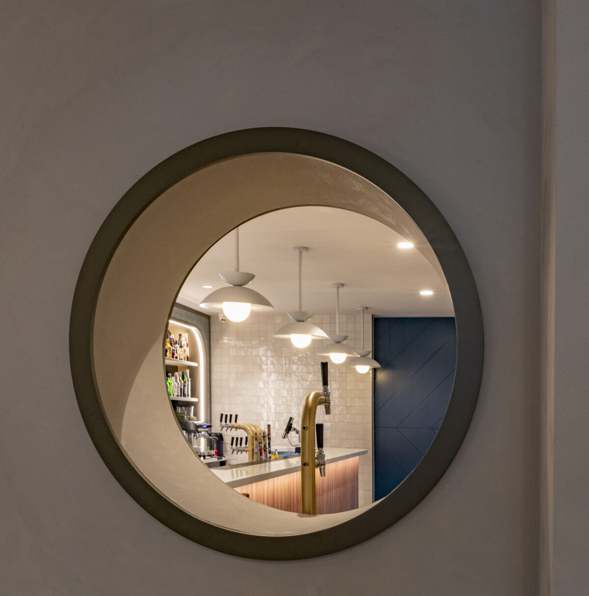 A circular wall opening frames a precise glimpse of the bar, transforming a functional threshold into a sculptural moment.