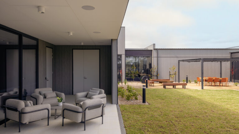 A sheltered outdoor lounge opens directly to the central garden. Deep, low chairs and a compact coffee table create a conversational setting, while the covered edge provides shade, weather protection and a gentle threshold between indoor comforts and the landscape beyond.