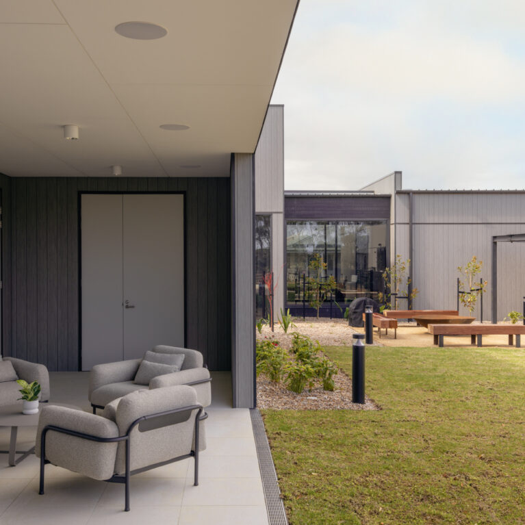 A sheltered outdoor lounge opens directly to the central garden. Deep, low chairs and a compact coffee table create a conversational setting, while the covered edge provides shade, weather protection and a gentle threshold between indoor comforts and the landscape beyond.