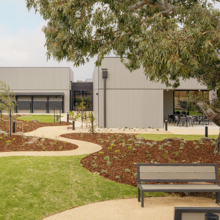 Curving paths stitch together lawns, native planting and shaded seating. The clubhouse reads as a series of calm pavilions, while mature eucalypts lend character and scale. It’s an easy landscape to stroll, pause and meet neighbours in.
