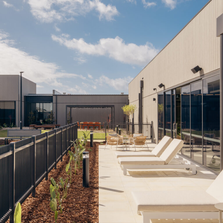 A calm, private sun deck edges the pool hall, stepping out to citrus-toned planting and views of the courtyard. Generous loungers, café settings and a low fence keep the space sociable yet secure—perfect for a slow morning or post-swim pause.