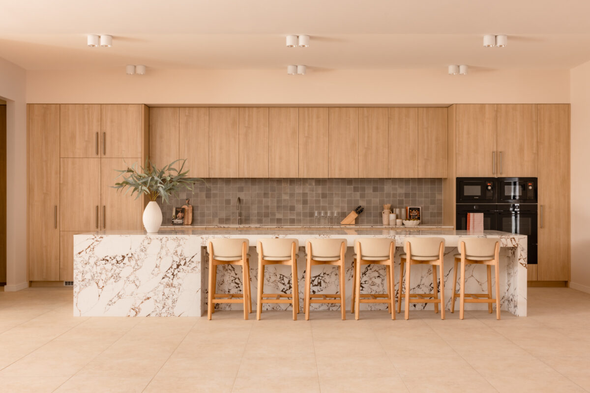 A generous island anchors the residents’ kitchen, pairing a boldly veined stone with pale timber joinery. Soft task lighting washes a square-tiled splashback, while integrated appliances and slimline stools turn the space into a relaxed hub for cooking, classes and communal dining.