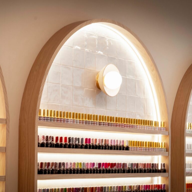 A closer look at the nail polish display reveals arched niches that merge practicality with elegance. Warm backlighting and soft oak framing turn a simple storage solution into a striking visual feature that draws the eye immediately.