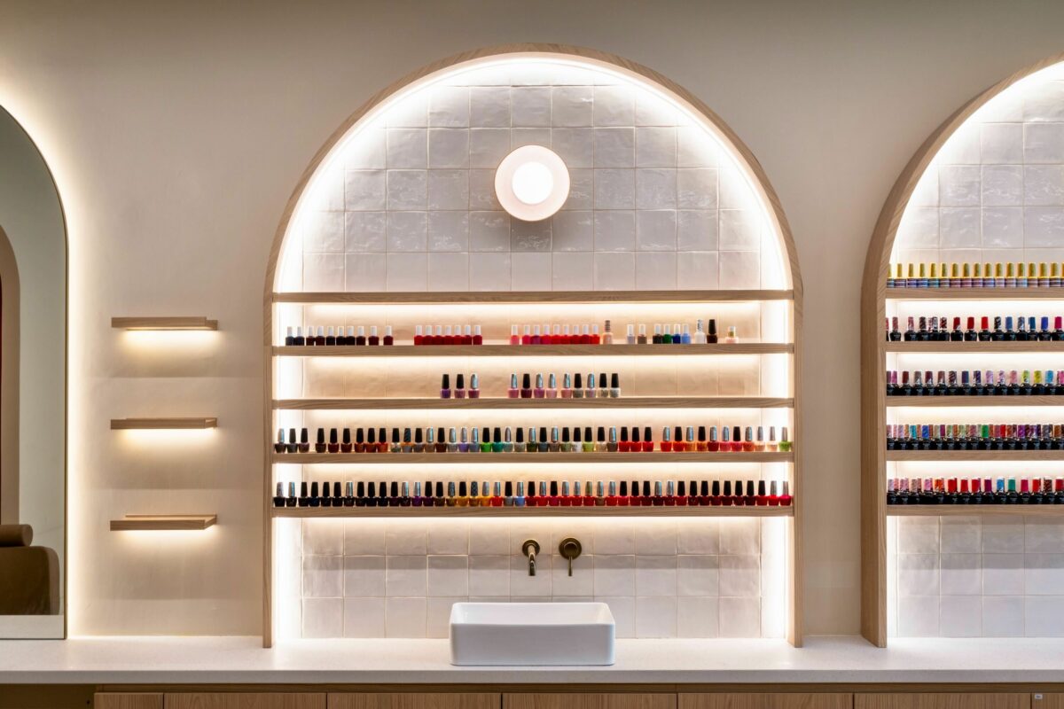 A refined manicure back counter combines open nail polish displays with a practical wash basin, balancing beauty and function. The softly lit arched niches highlight the bottles’ vibrant colors, while the integrated counter supports smooth operations for staff and clients.