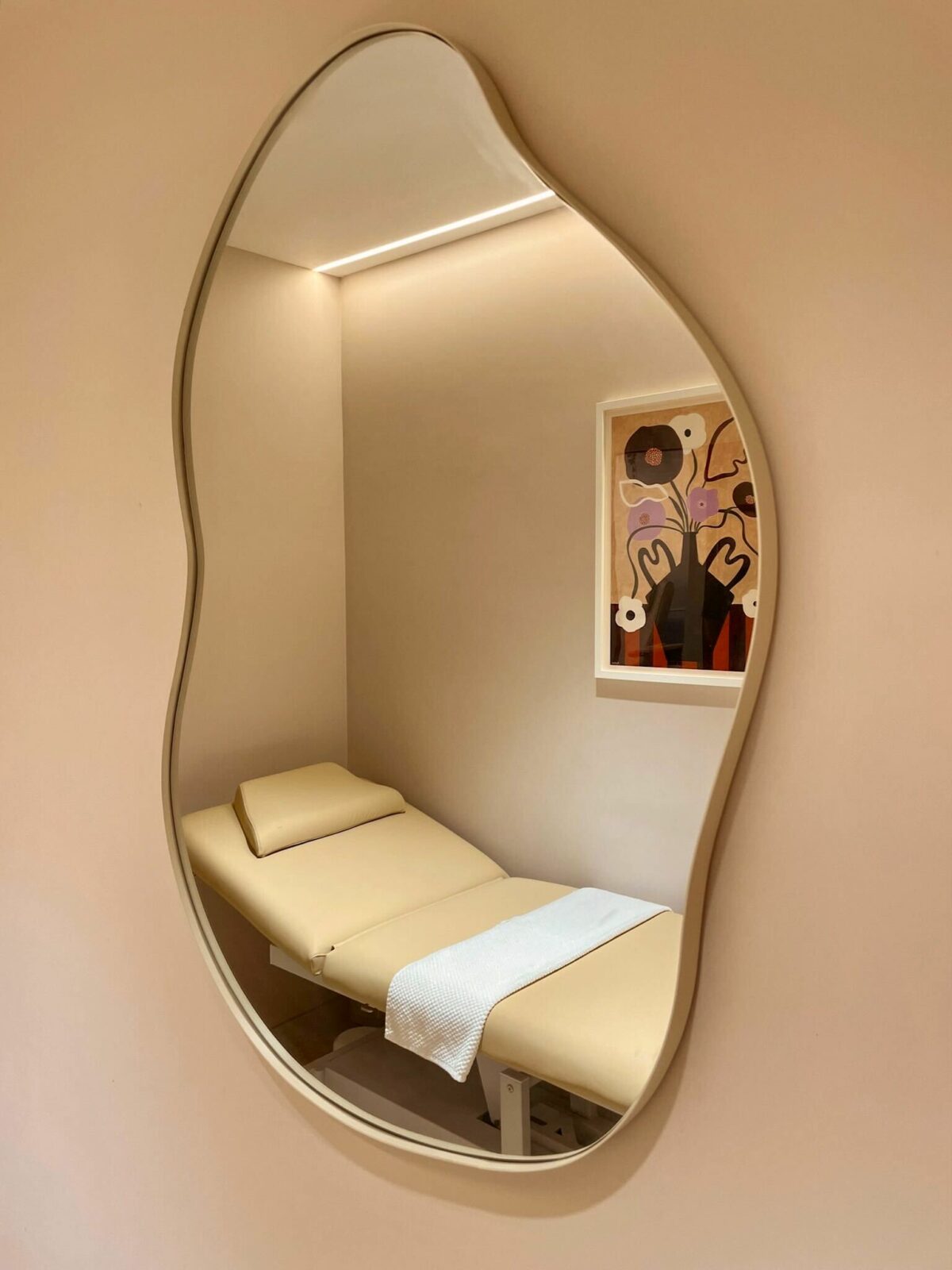 This treatment room evokes serenity with its soft, neutral palette and calming textures. The organic mirror shape adds playfulness, while indirect lighting enhances the soothing ambiance, creating an intimate environment for personalized beauty treatments.