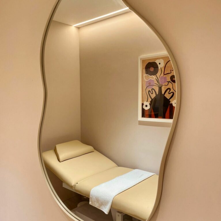This treatment room evokes serenity with its soft, neutral palette and calming textures. The organic mirror shape adds playfulness, while indirect lighting enhances the soothing ambiance, creating an intimate environment for personalized beauty treatments.