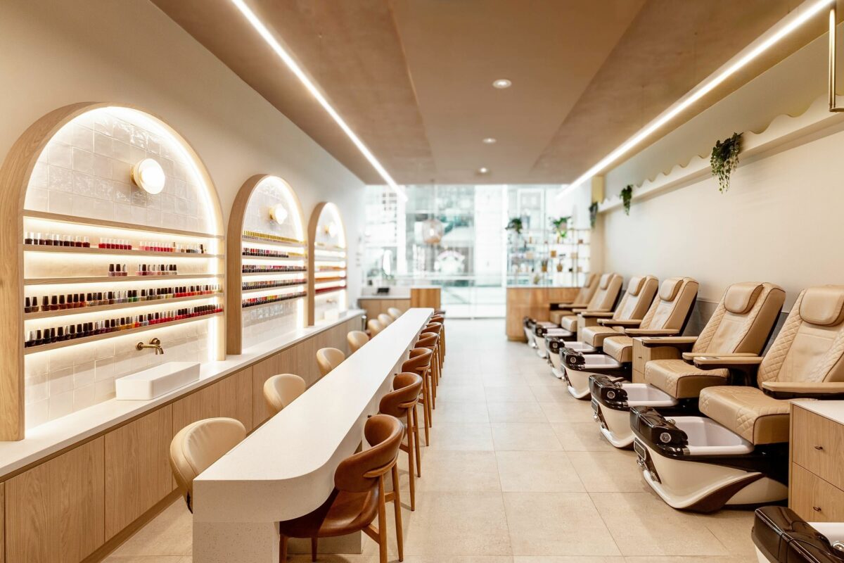 This wide-angle view showcases the salon’s full layout, with manicure stations running parallel to a row of plush pedicure chairs. Thoughtful zoning and consistent design language create a harmonious, flowing space that feels both intimate and generously open.