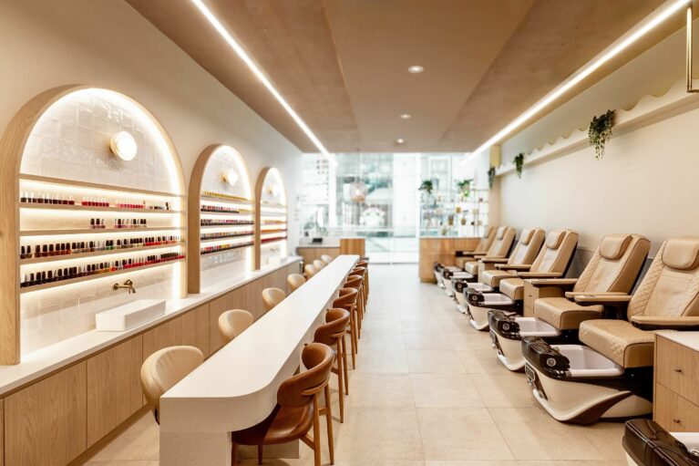 This wide-angle view showcases the salon’s full layout, with manicure stations running parallel to a row of plush pedicure chairs. Thoughtful zoning and consistent design language create a harmonious, flowing space that feels both intimate and generously open.