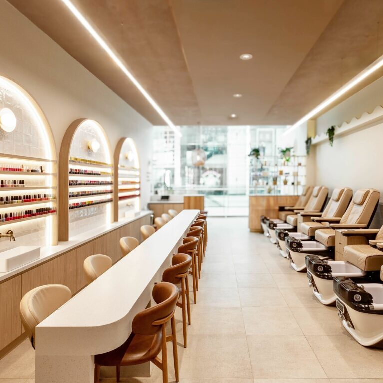 This wide-angle view showcases the salon’s full layout, with manicure stations running parallel to a row of plush pedicure chairs. Thoughtful zoning and consistent design language create a harmonious, flowing space that feels both intimate and generously open.