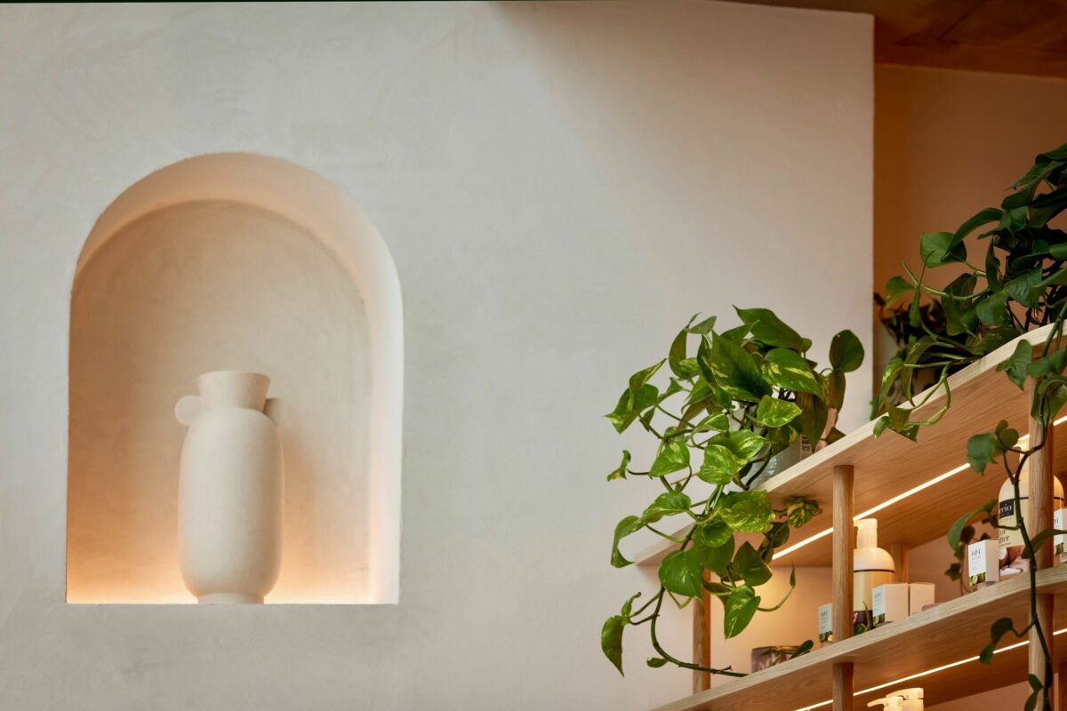 A softly illuminated alcove brings sculptural depth to the wall, showcasing a minimalist ceramic vase. Paired with trailing greenery from the nearby shelving, it introduces organic warmth and creates a serene, gallery-like focal point within the space.