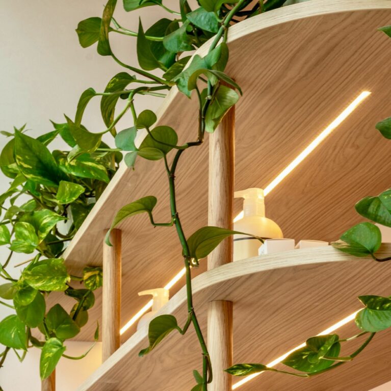 Subtle integrated lighting elevates the shelving, highlighting the display items while emphasizing the natural grain of the timber. This built-in illumination adds warmth and depth, balancing functionality with an inviting, boutique-like ambiance that enhances the overall salon experience.