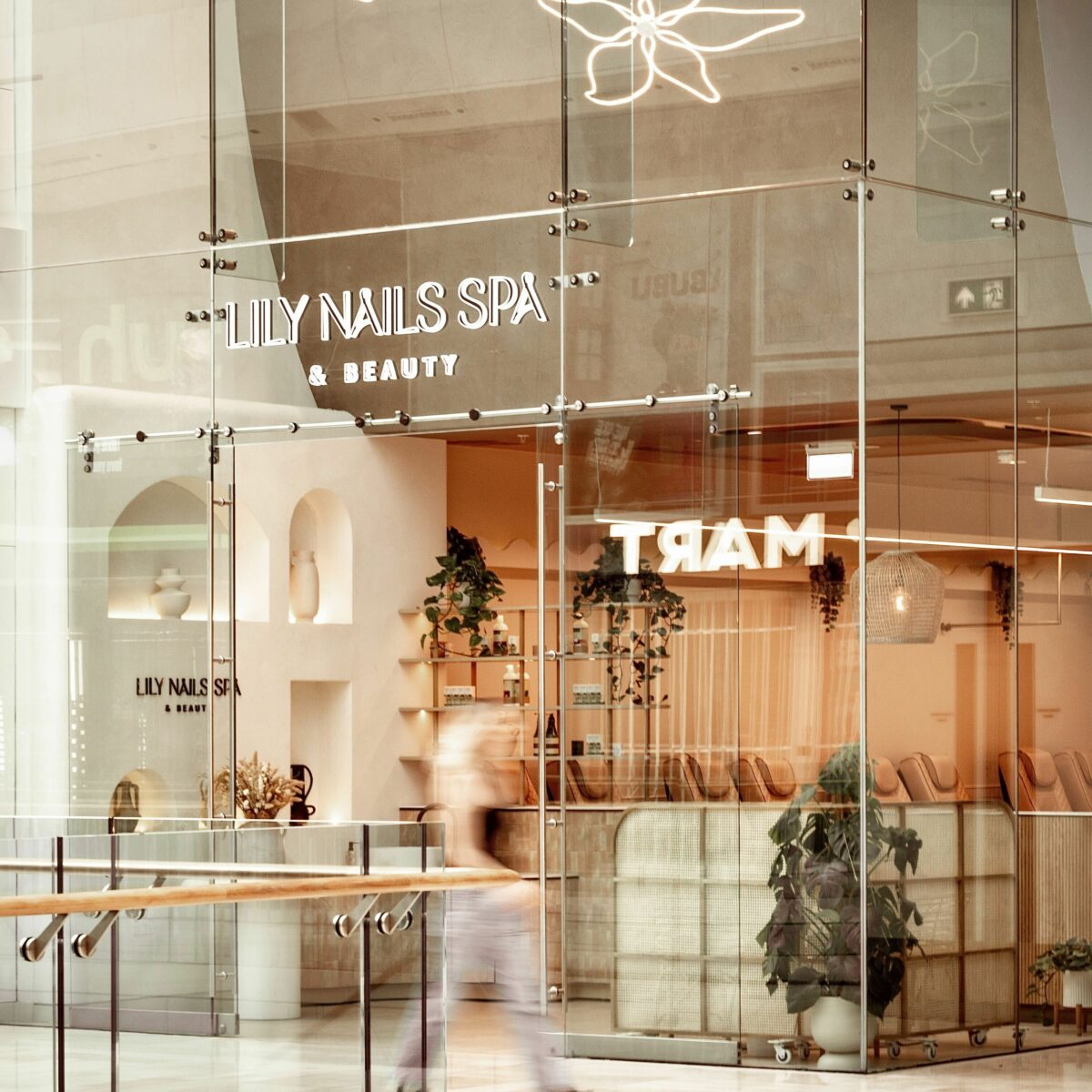 The open glass shopfront creates an inviting connection between the salon interior and the shopping mall, allowing natural light to enhance the warm neutral palette inside.