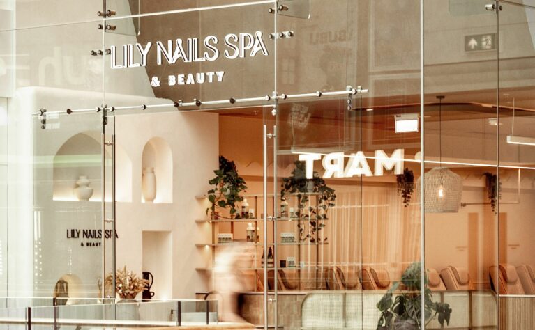 The open glass shopfront creates an inviting connection between the salon interior and the shopping mall, allowing natural light to enhance the warm neutral palette inside.