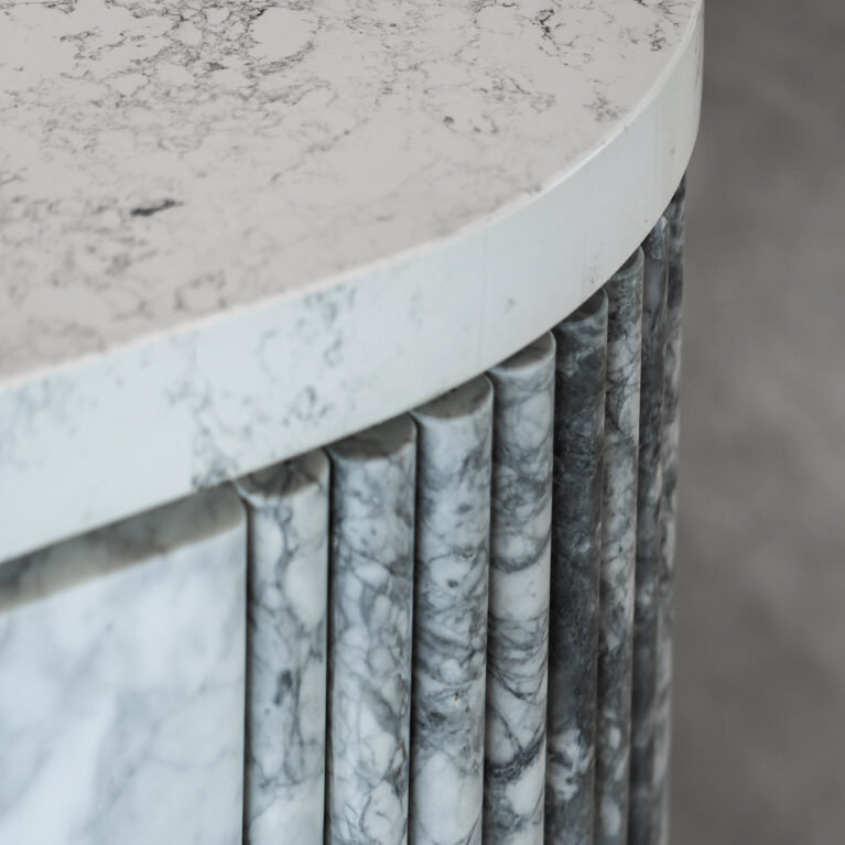 A close-up of the island reveals the exquisite veining of Calacatta marble, accentuated by vertical fluted detailing along the base. This refined texture adds a dynamic, tactile quality to the kitchen’s luxurious design.