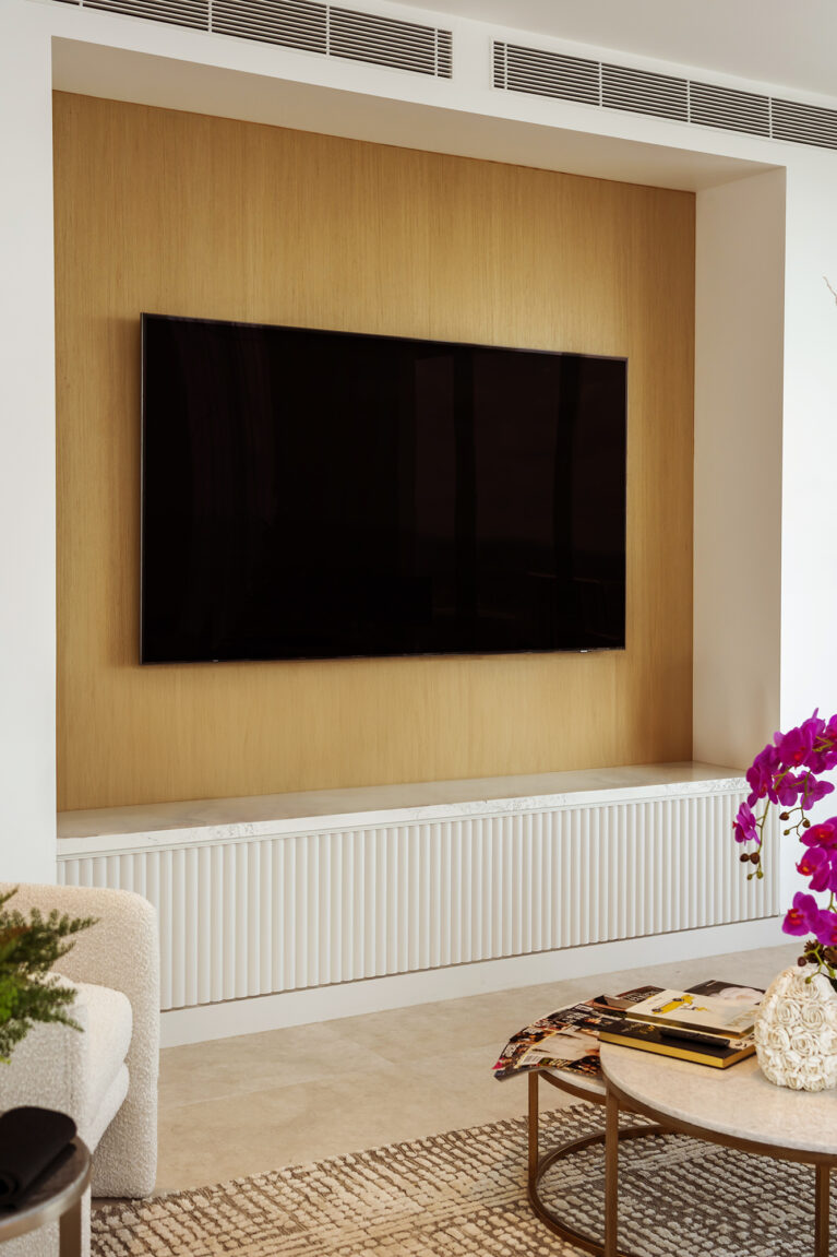 The entertainment wall features light oak paneling and a Calacatta marble-topped console, blending functionality with elegance. The warm tones and clean lines offer a contemporary, stylish setup for the living area.