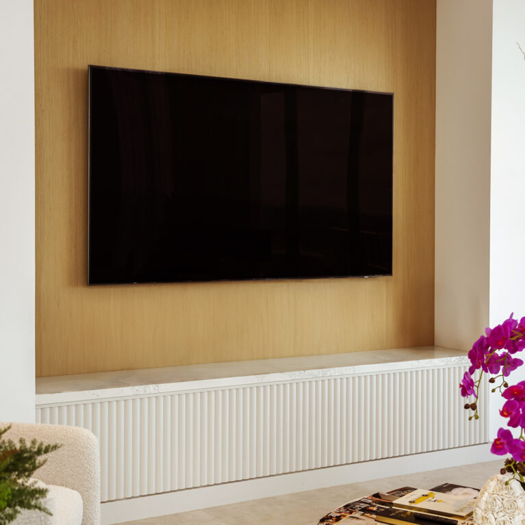 The entertainment wall features light oak paneling and a Calacatta marble-topped console, blending functionality with elegance. The warm tones and clean lines offer a contemporary, stylish setup for the living area.