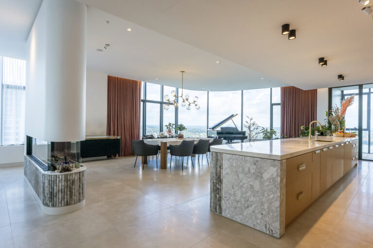 The open-plan kitchen and dining area, framed by floor-to-ceiling windows, showcases Calacatta marble and oak finishes, enhancing the natural light and expansive views. The design invites seamless transitions between cooking, dining, and entertaining.