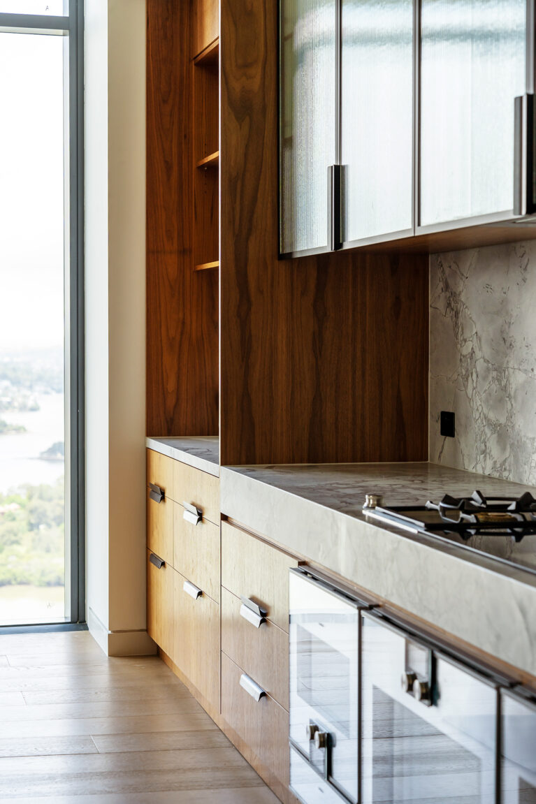 A detailed view of the kitchen, featuring walnut cabinetry, a honed marble countertop, and fluted glass cabinets for an elegant, modern aesthetic.