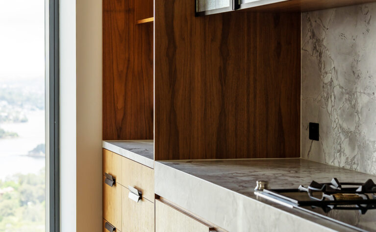 A detailed view of the kitchen, featuring walnut cabinetry, a honed marble countertop, and fluted glass cabinets for an elegant, modern aesthetic.