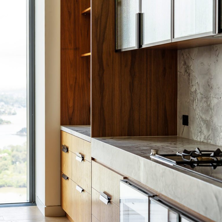 A detailed view of the kitchen, featuring walnut cabinetry, a honed marble countertop, and fluted glass cabinets for an elegant, modern aesthetic.