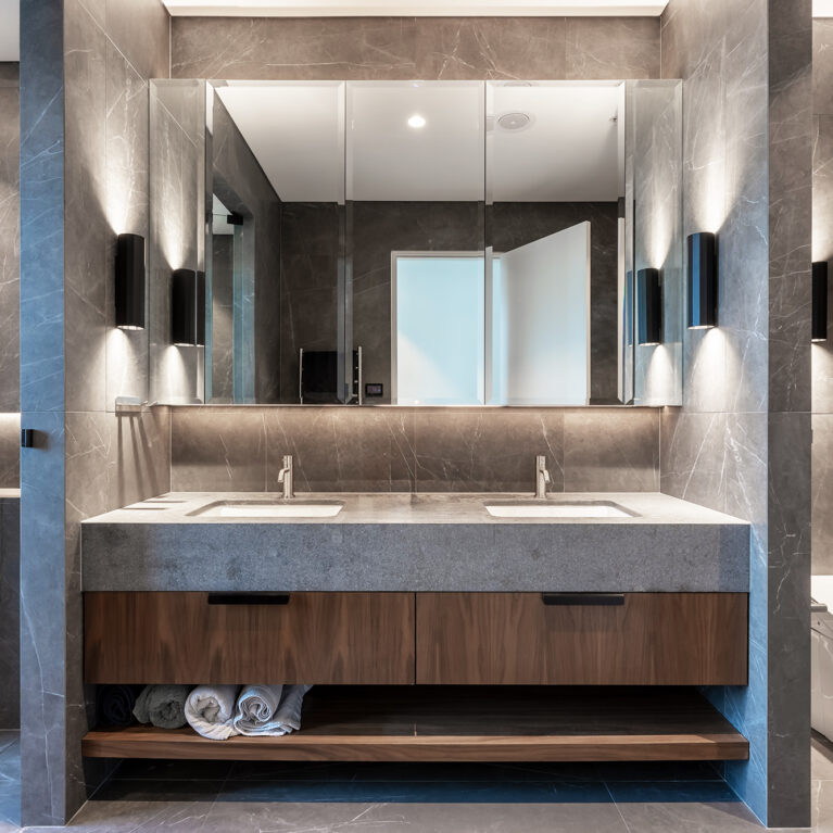 A luxurious master ensuite bathroom with Pietra Grey tiles, American Walnut cabinetry, and soft integrated lighting.