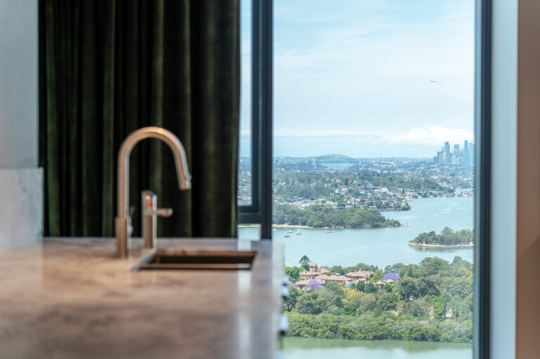 A serene kitchen view with luxurious finishes and a stunning backdrop of Sydney's skyline, showcasing premium materials and a refined design.