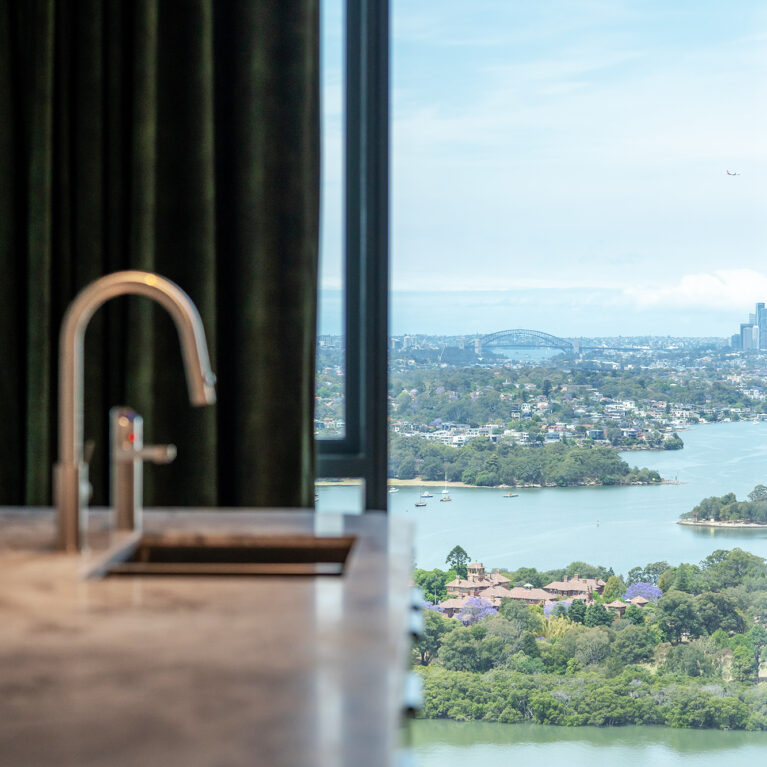 A serene kitchen view with luxurious finishes and a stunning backdrop of Sydney's skyline, showcasing premium materials and a refined design.