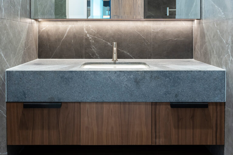 A refined guest ensuite basin with elegant stone tiles, walnut cabinetry, and ambient lighting, combining function with style.