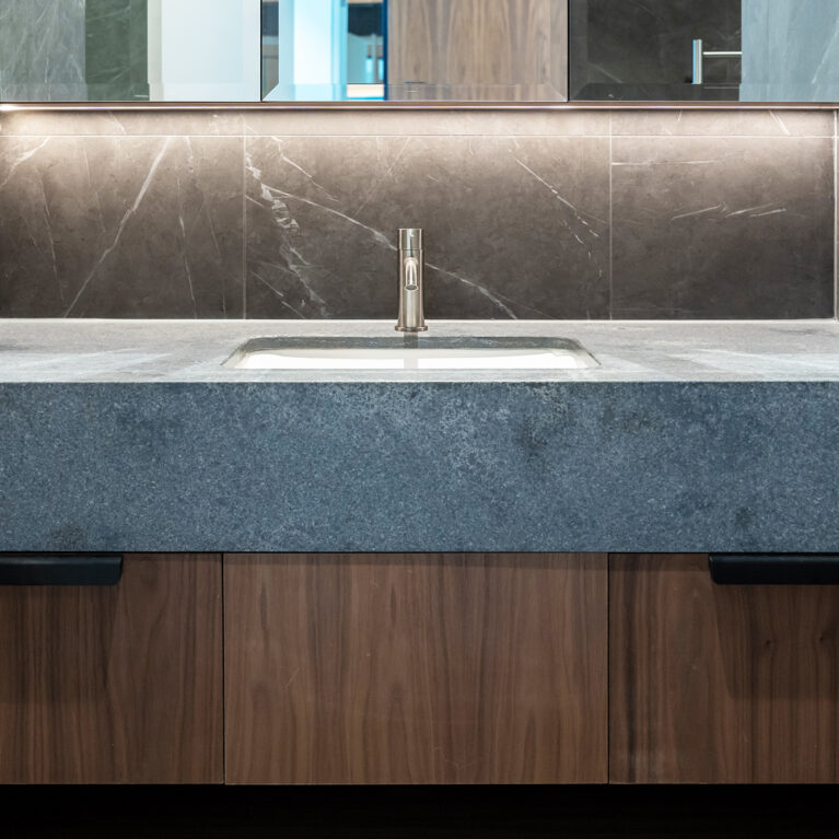 A refined guest ensuite basin with elegant stone tiles, walnut cabinetry, and ambient lighting, combining function with style.