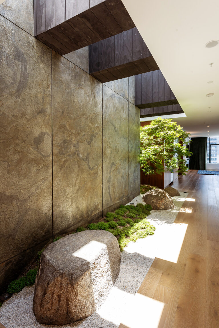 A Japanese-inspired courtyard with natural stone, textured walls, and greenery, creating a peaceful retreat along the corridor.