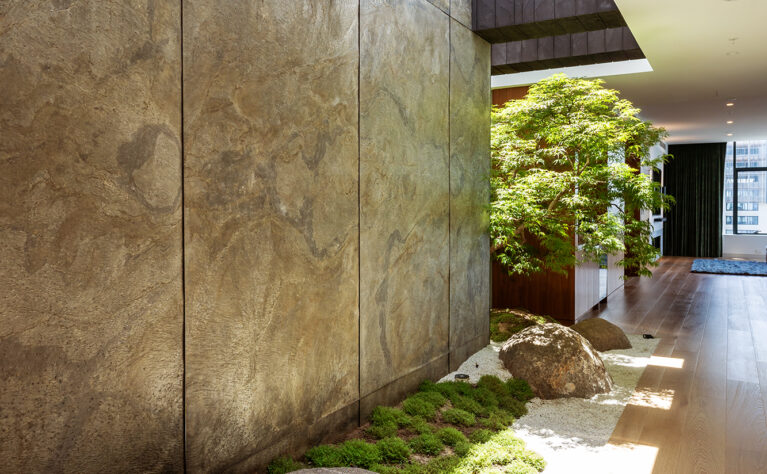 A Japanese-inspired courtyard with natural stone, textured walls, and greenery, creating a peaceful retreat along the corridor.