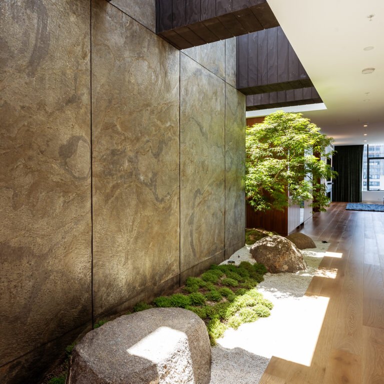 A Japanese-inspired courtyard with natural stone, textured walls, and greenery, creating a peaceful retreat along the corridor.