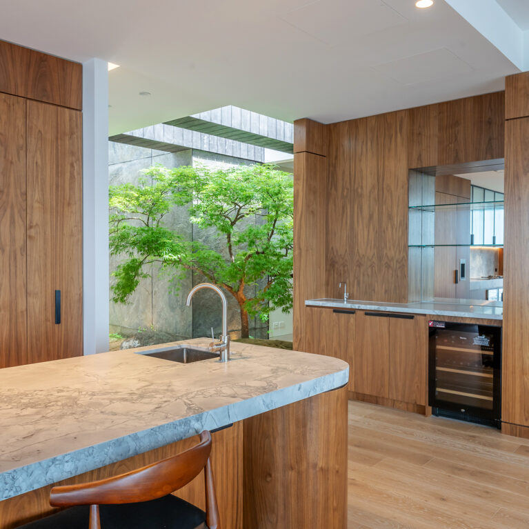 An elegant kitchen and bar area that flows seamlessly into a serene Japanese-inspired courtyard, blending luxury and nature.