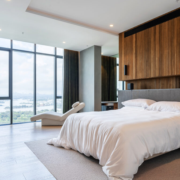 A serene master bedroom with walnut ribbed walls, luxurious furnishings, and floor-to-ceiling windows showcasing panoramic city views.