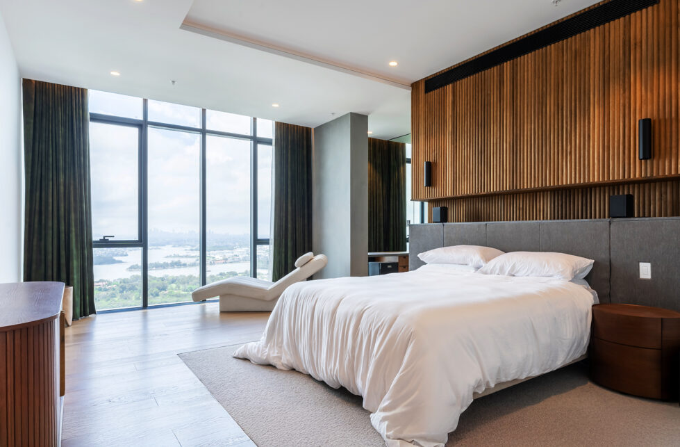 A serene master bedroom with walnut ribbed walls, luxurious furnishings, and floor-to-ceiling windows showcasing panoramic city views.