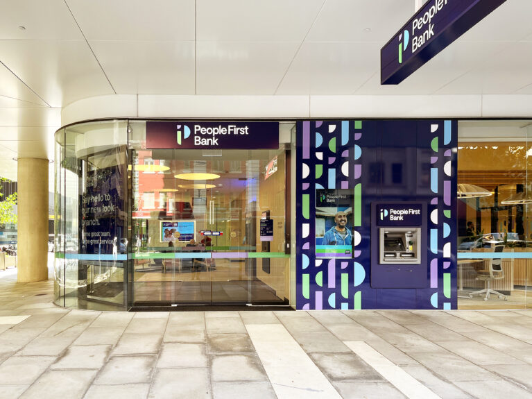 The bank's facade combines lilac and deep purple accent panels with prominent logos and a glass entry, offering visibility into the welcoming, modern lobby.