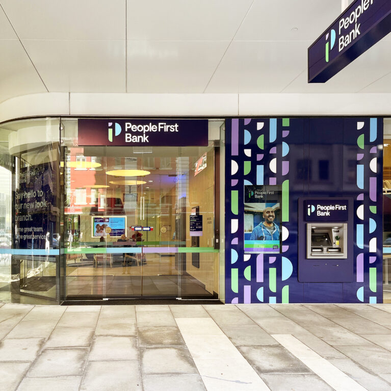 The bank's facade combines lilac and deep purple accent panels with prominent logos and a glass entry, offering visibility into the welcoming, modern lobby.