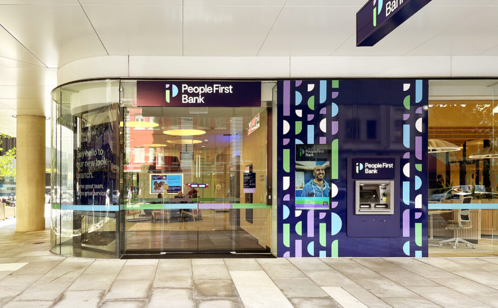 The bank's facade combines lilac and deep purple accent panels with prominent logos and a glass entry, offering visibility into the welcoming, modern lobby.