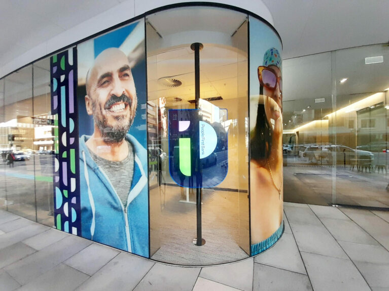 The glass facade highlights vibrant portraits and bold graphic elements, reflecting inclusivity and community pride. Natural light floods the space, inviting passersby to explore the interior’s welcoming atmosphere and innovative design philosophy.