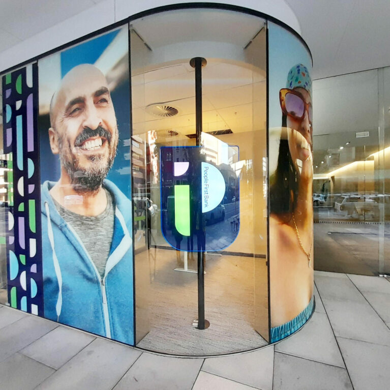 The glass facade highlights vibrant portraits and bold graphic elements, reflecting inclusivity and community pride. Natural light floods the space, inviting passersby to explore the interior’s welcoming atmosphere and innovative design philosophy.