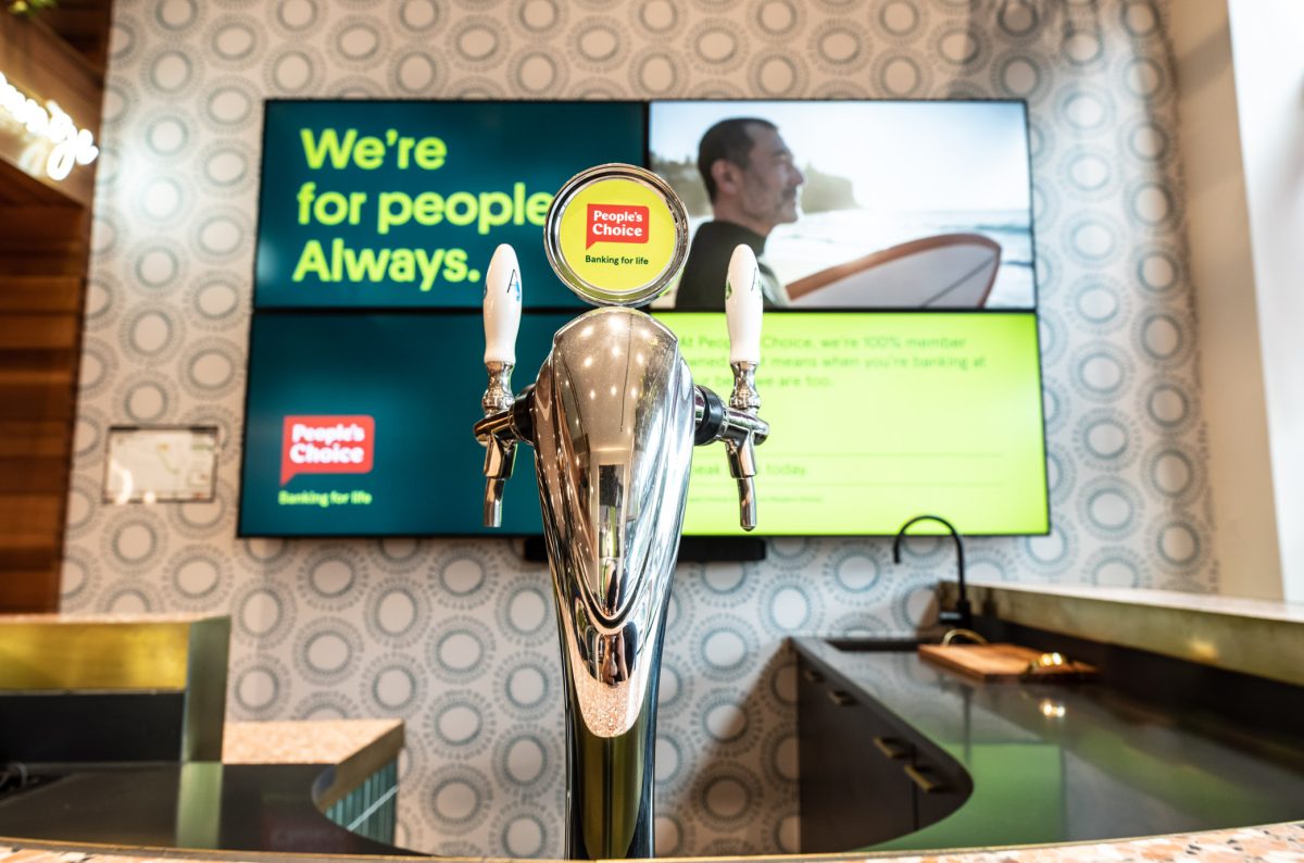 A close-up of the bar tap and digital displays at People’s Choice bank’s lounge area, blending classic design with modern branding.