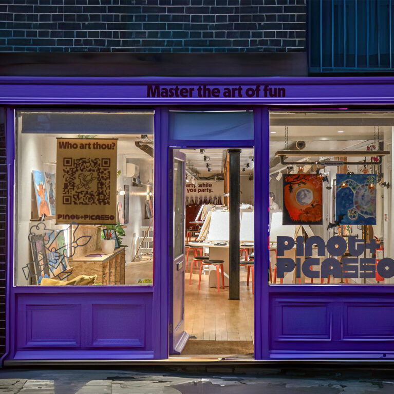 The inviting storefront glows with energy, drawing in guests with its bold purple accents and warm interior lighting. Playful typography and quirky signage set the stage for a creative space where art meets fun in a vibrant, social setting.