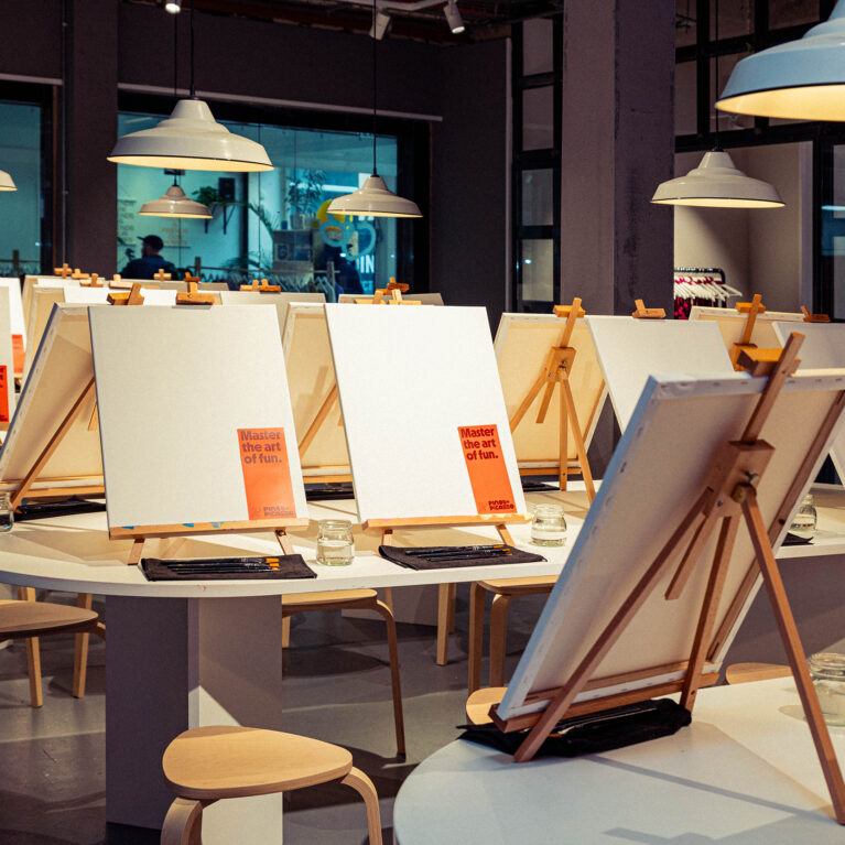 Blank canvases and neatly arranged easels set the stage for a hands-on artistic experience. With soft lighting, natural wood furniture, and an inviting atmosphere, this creative hub is ready to welcome guests into a space where imagination comes to life.