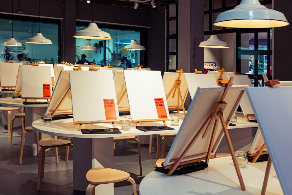 Blank canvases and neatly arranged easels set the stage for a hands-on artistic experience. With soft lighting, natural wood furniture, and an inviting atmosphere, this creative hub is ready to welcome guests into a space where imagination comes to life.