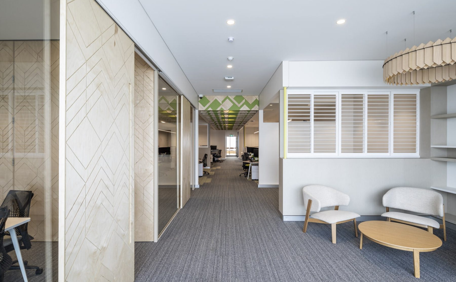 Corporate breakout furniture, white plantation shutters, acoustic felt lighting, sliding timber doors, glazed office partitions, commercial linear layout, geometric ceiling acoustic baffles, grey carpet tiles.