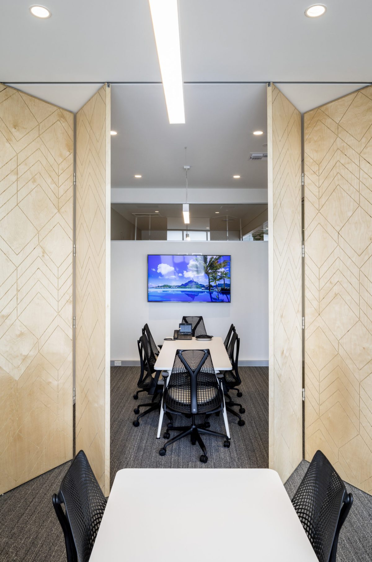 Acoustic operable walls, folding timber panels, corporate boardroom layout, mesh office chairs, recessed linear lighting, acoustic commercial carpeting, geometric routing, agile workplace.