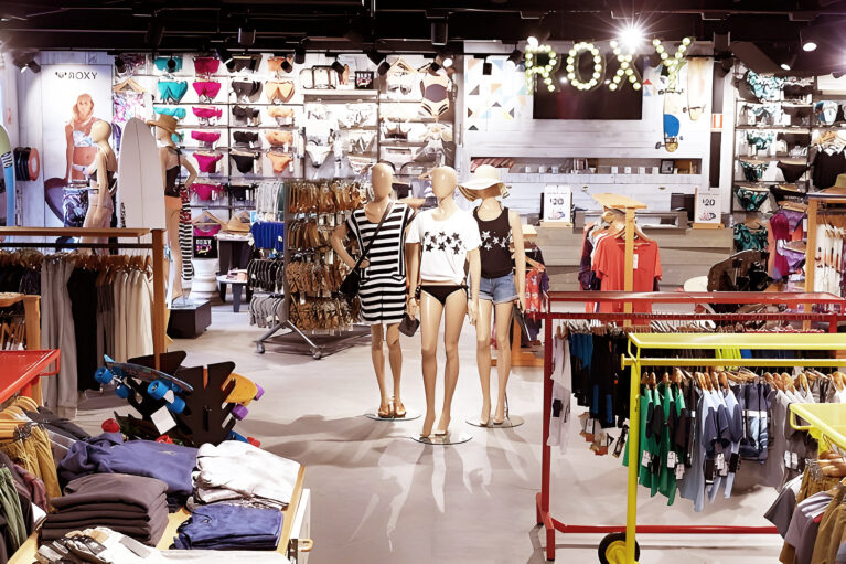 The Roxy section features bold displays with swimwear, casual outfits, and accessories, all enhanced by striking lighting and playful accents. Mannequins showcase curated looks, while the bright branding and organized layout invite customers to explore effortlessly.