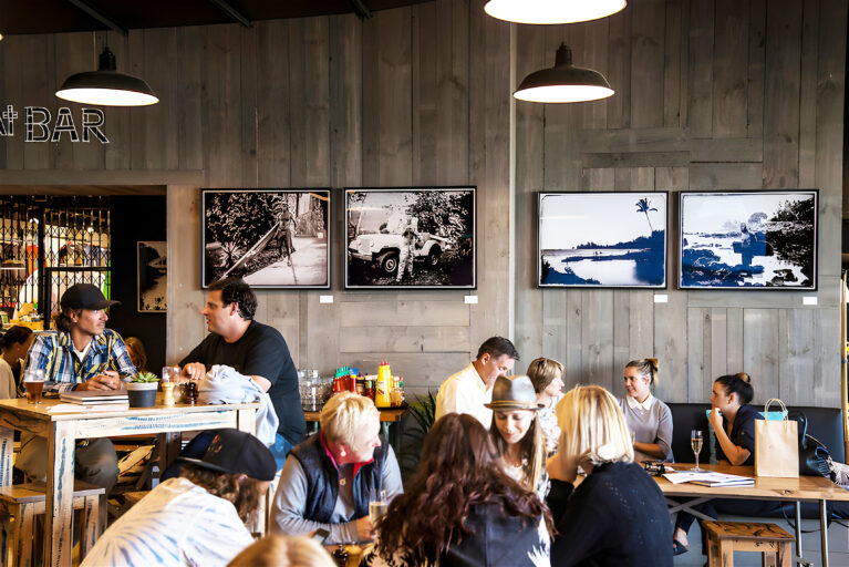 The in-store café offers a relaxed social setting, featuring reclaimed wood paneling, surf photography, and warm lighting. Guests enjoy casual dining surrounded by surf-inspired decor, making the space a natural gathering point for locals and visitors alike.